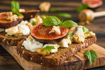 Healthy toasts with rye bread, fresh figs, honey, walnuts, mint leaves and cheese on the wooden board