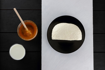 Homemade cheese and honey on a wooden background, soft cheese on a black plate, minimalism, wooden...