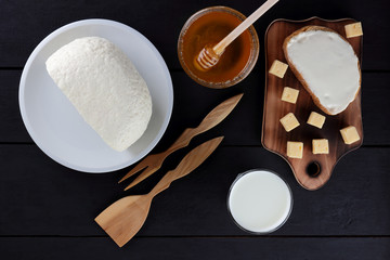 Cheese and honey on a dark wooden background, white plate, minimalism, wooden cutlery, honey, kefir in a glass, copy space, a sandwich with soft cheese, American cuisine