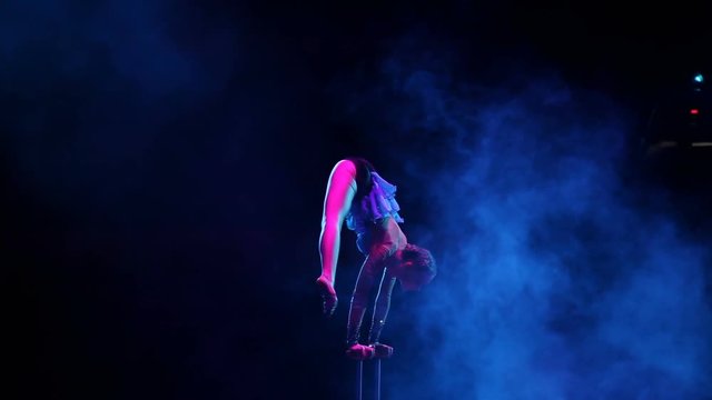 Young flexible acrobat girl executes tricks on a cube in circus