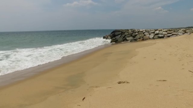 A scenic view of a beach with waves hitting the yellow sand shore and rocks.