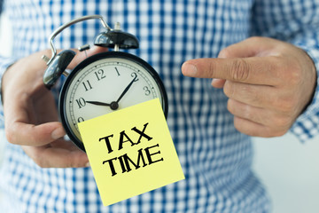 Hand Holding Alarm Clock and Pointing TAX TIME