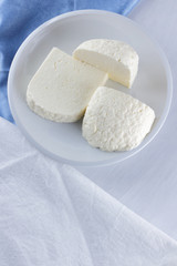 Cheese on a white background, soft cheese on a white plate, a glass of yogurt, minimalism, copy space, dairy products on a white blue napkin, French breakfast, American cuisine