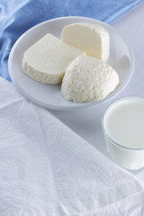 Cheese on a white background, soft cheese on a white plate, a glass of yogurt, minimalism, copy space, dairy products on a white blue napkin, French breakfast, American cuisine