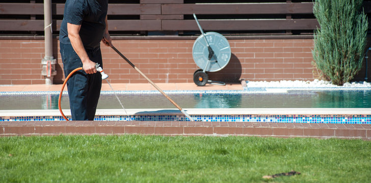 Man clean swimming pool with hose in hands outdoors