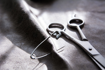 Scissors and a pin on a gray fabric with a rough surface
