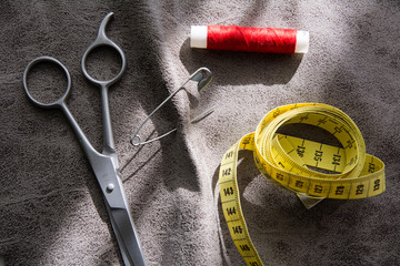 Measuring tape, scissors and reel of red thread on gray fabric