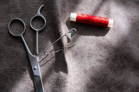 Scissors and reel of red thread on gray fabric
