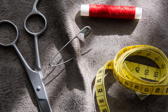 Measuring tape, scissors and reel of red thread on gray fabric