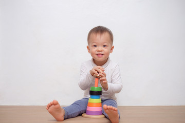 Cute little Asian 18 months / 1 year old toddler baby boy child play with colorful wooden pyramid...