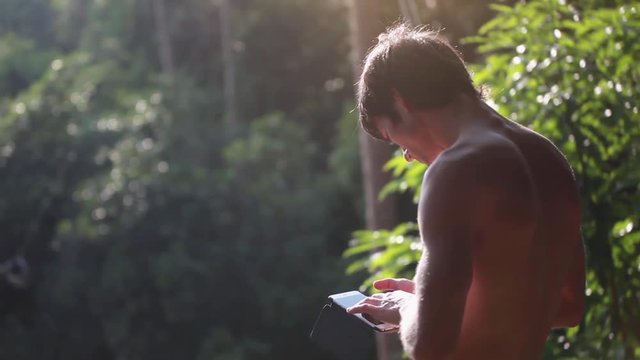 Young man traveler flooded with sunlight in the jungle uses a telephone. 1920x1080