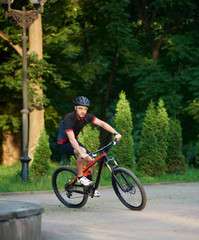 Sporty male cyclist in sportswear training on bike, riding paved park alley. Muscle sportsman getting ready for contest. Concept of healthy lifestyle