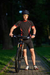 Obraz premium Sporty smiling man bicyclist walking near bicycle happy to begin morning with training. Sportsman having fun exercising outdoors. Concept of healthy lifestyle, new beginning