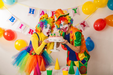Clowns are a boy and a girl in bright costumes at the child's birthday. A table with refreshments and a cake. The explosion of emotions and the fun of the circus. greed and desire to eat cake
