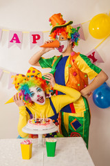 Clowns are a boy and a girl in bright costumes at the child's birthday. A table with refreshments and a cake. The explosion of emotions and the fun of the circus. greed and desire to eat cake