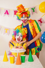 Clowns are a boy and a girl in bright costumes at the child's birthday. A table with refreshments and a cake. The explosion of emotions and the fun of the circus. greed and desire to eat cake