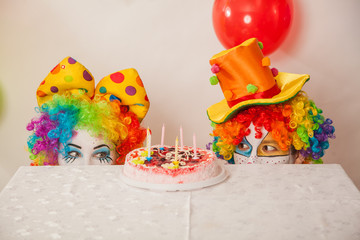 Clowns are a boy and a girl in bright costumes at the child's birthday. A table with refreshments and a cake. The explosion of emotions and the fun of the circus. greed and desire to eat cake