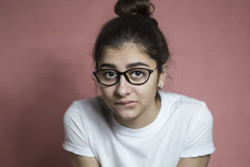 A thoughtful girl in glasses looks at the camera. A young woman thinks about the idea by biting her lower lip.