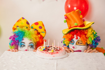 Clowns are a boy and a girl in bright costumes at the child's birthday. A table with refreshments and a cake. The explosion of emotions and the fun of the circus. greed and desire to eat cake