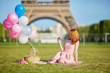 Woman in pink dress with bunch of balloons having picnic near the Eiffel tower in Paris