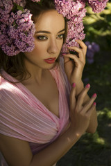 Spring portrait of young beautiful girl with bunch of flowers (pink lilac) around her hair in the garden