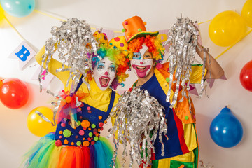 Clown girl and clown boy in bright costumes at the baby's birthday party. The explosion of emotions and the fun of the circus. Paper disco made of silver paper