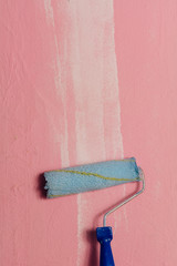 Paint roller leaning against a pink wall, with a white brushstroke