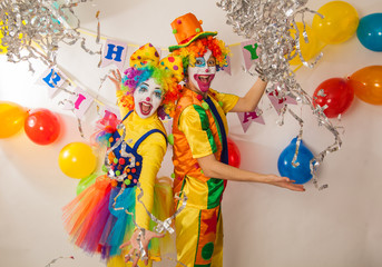 Clown girl and clown boy in bright costumes at the baby's birthday party. The explosion of emotions and the fun of the circus. Paper disco made of silver paper