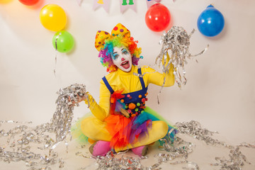 A clown girl in a bright suit at the baby's birthday party. The explosion of emotions and the fun of the circus. Paper disco made of silver paper