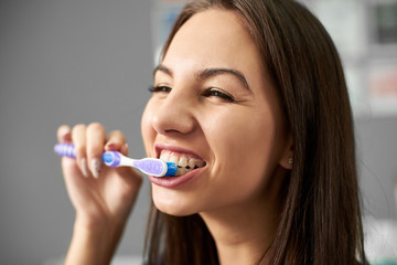 Obraz premium Young attractive brunette is cleaning her teeth with a toothbrush and smiling and being happy about this.