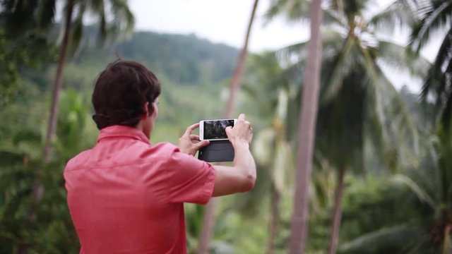 Young man with cellphone takes photo in a jungle on his vacation trip. 1920x1080