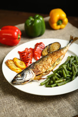 Healthy and proper food, grilled fish and vegetables with lemon and green beans on a white plate. On the background of pepper, burlap and wooden table. Low-calorie food
