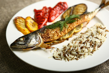 Healthy and proper food, grilled fish and vegetables with lemon and black and white rice on a white plate. Against the background of sacking and a wooden table. Low-calorie food