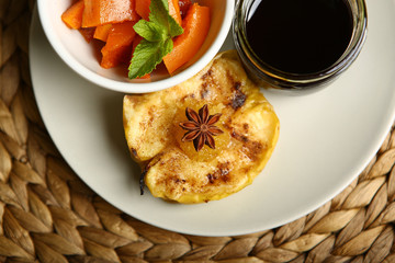 On the plate is a baked pumpkin, an apple and a glass jar with honey, near cinnamon, anise, mint. Wicker substrate and wooden table, composition. Close-up