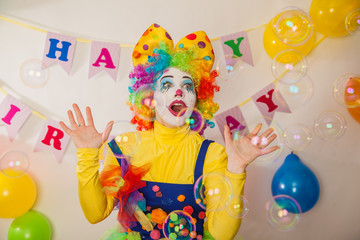 A clown girl in a bright suit at the baby's birthday party. The explosion of emotions and the fun of the circus. The sea of soap bubbles
