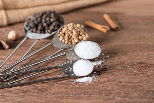 Food ingredient for cooking on a wooden board. Measuring spoons with salt, sugar, coriander seed and black pepper.