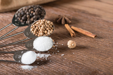 Food ingredient for cooking on a wooden board. Measuring spoons with salt, sugar, coriander seed and black pepper.