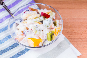 Delicious fruit salad with yogurt in a glass cup on a wooden table - top view, fruit diet