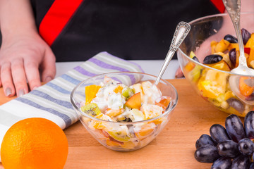 Tropical fruit salad with yoghurt in a glass cup on a wooden table - fruit diet