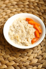 Low-calorie porridge for a healthy diet and lifestyle. Barley with honey and bits of orange pumpkin in a deep white plate. Dark background, wooden table and wicker stand