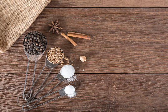 Food ingredient for cooking on a wooden board. Measuring spoons with salt, sugar, coriander seed and black pepper.