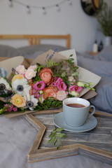 Fototapeta na wymiar Bouquet of flowers and a cup of tea on the bed