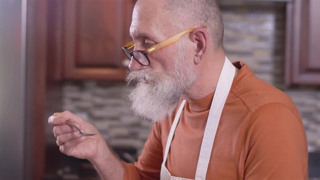 Close up profile shot of an old chef tasting his food