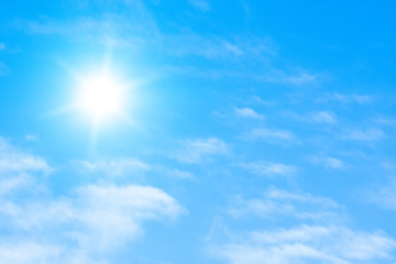 The sun with bright rays in the blue sky with white light clouds.