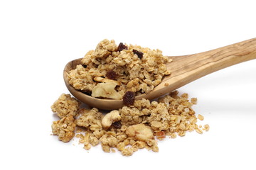 Crunchy granola, muesli pile with banana, pineapple slices, peanuts and raisins in wooden spoon isolated on white background