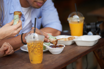 Close-up of couple dipping spring rolls into sauce at street cafe