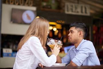 Young mixed couple sitting face-to-face during date at oudoor cafe