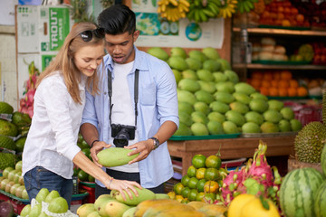 Obraz premium Young mixed couple of tourists choosing organic fruits at street market