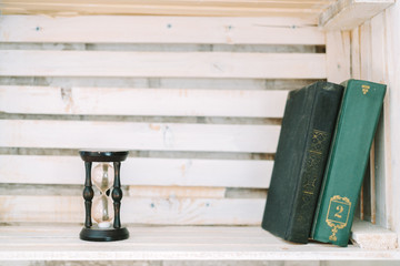 Obraz premium old books and sand clock lie on a white shelf.