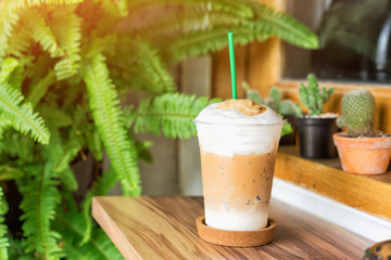 Cold coffee in plastic cup on wooden table at cafe.